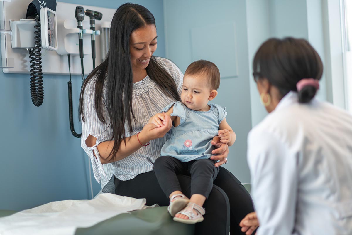 A mother holds her baby daughter on her lap while talking to a doctor.