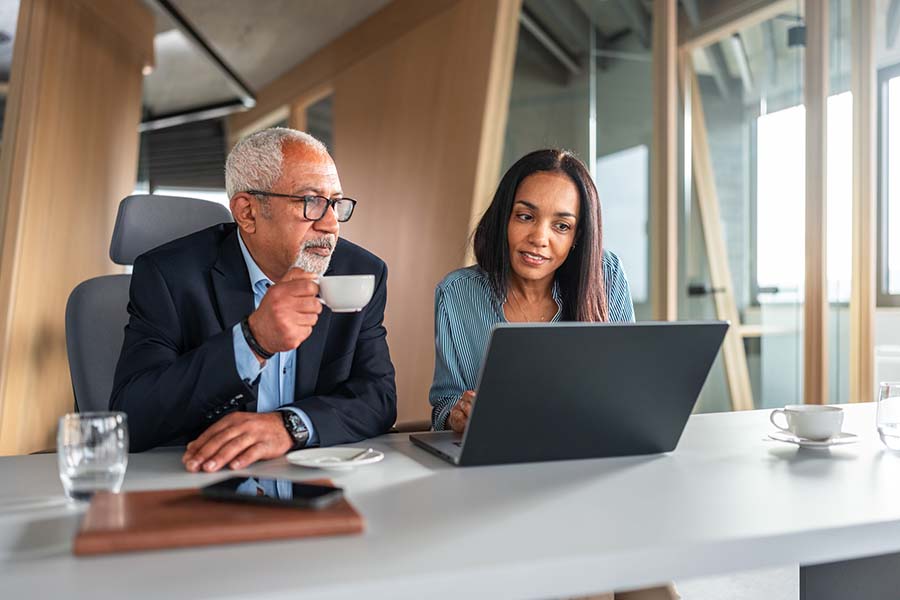 A man in an office looks at the laptop of a consultant, discussing Medicare benefit options for the company.