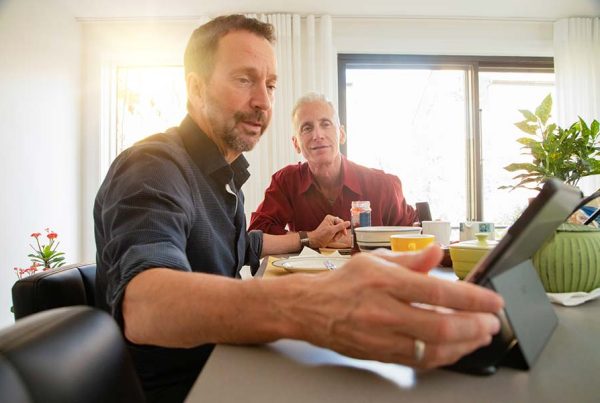 Senior gay couple having a lively conversation at breakfast about news on tablet.